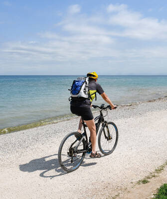 Une personne à vélo sur un chemin de terre longeant la plage du Croisic en Loire-Atlantique, avec l'océan Atlantique en arrière-plan sous un ciel bleu parsemé de nuages blancs.